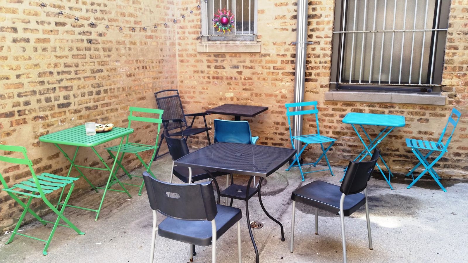 Brick-walled patio with green, teal and black folding cafe tables