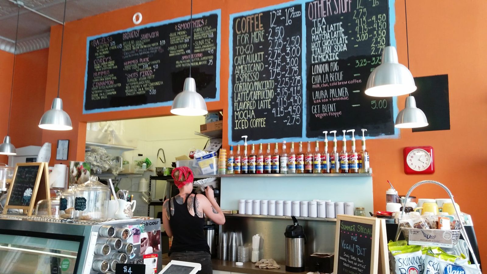 Orange counter with chalkboard menus, syrup bottles and barista working