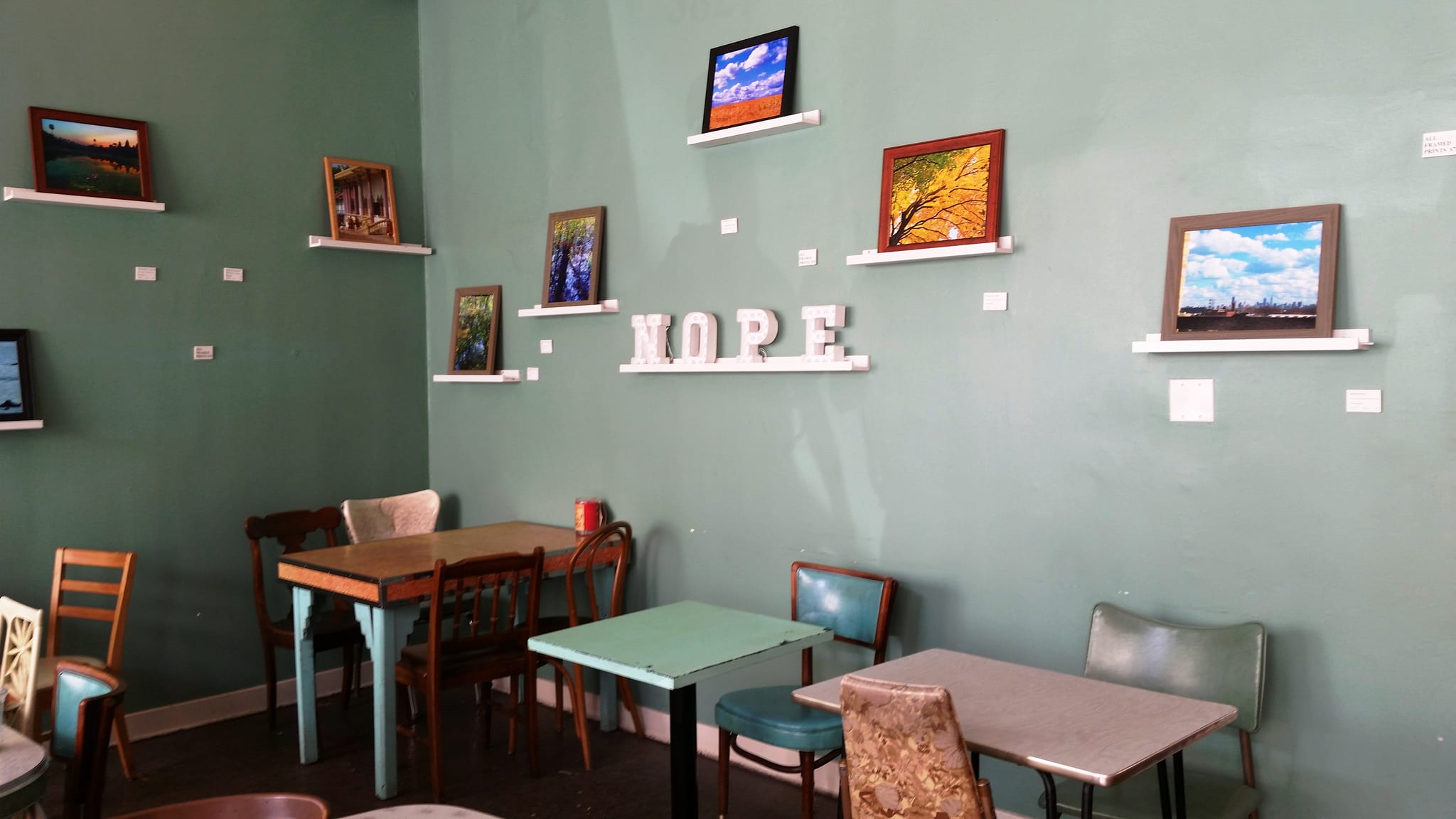 Green wall of framed photographs above vintage tables, letters spelling HOPE