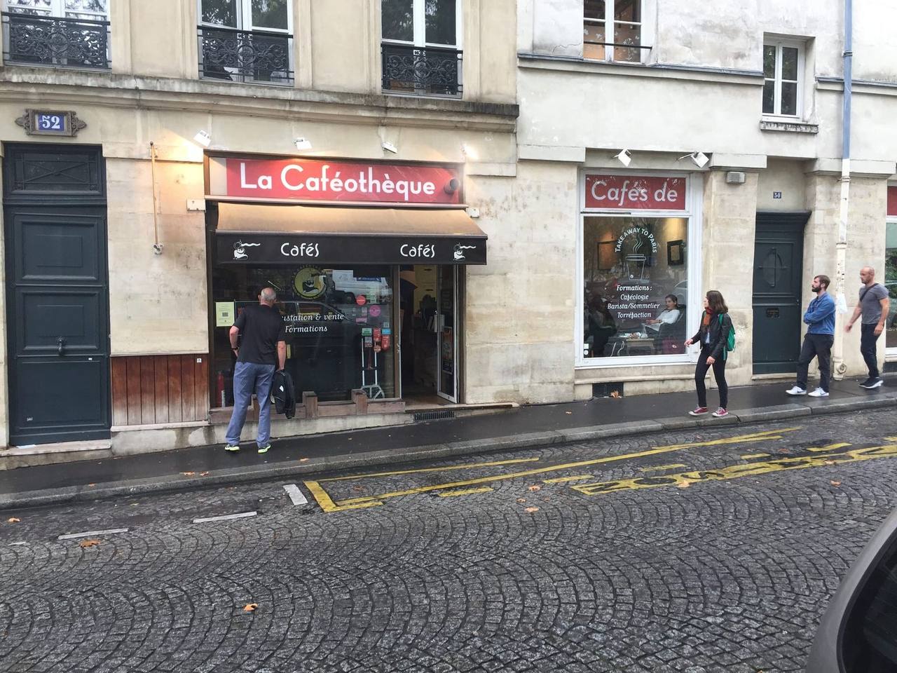 Red awning storefront on wet cobblestone Paris street with pedestrians
