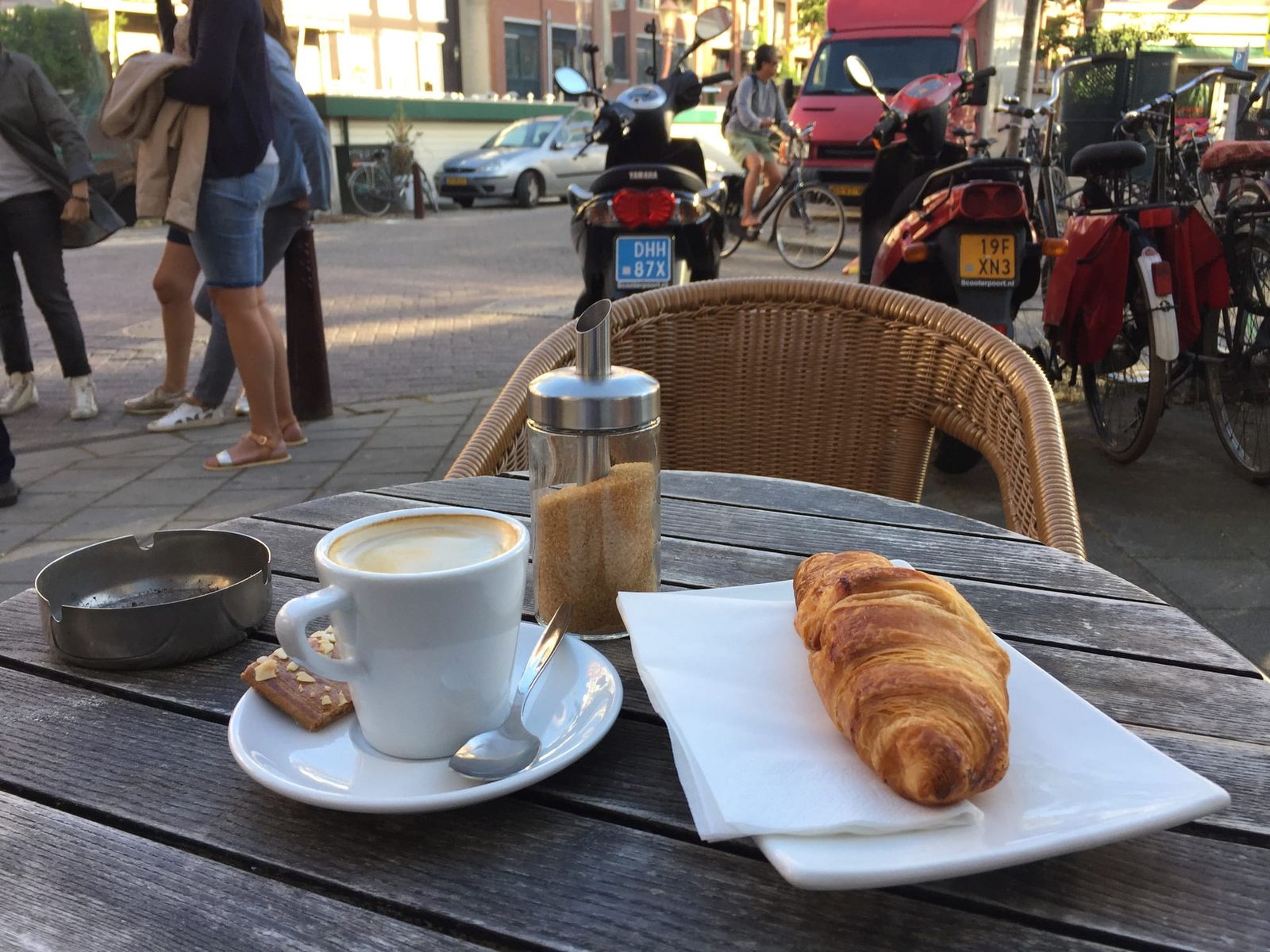 Cappuccino and croissant on outdoor table beside parked bikes