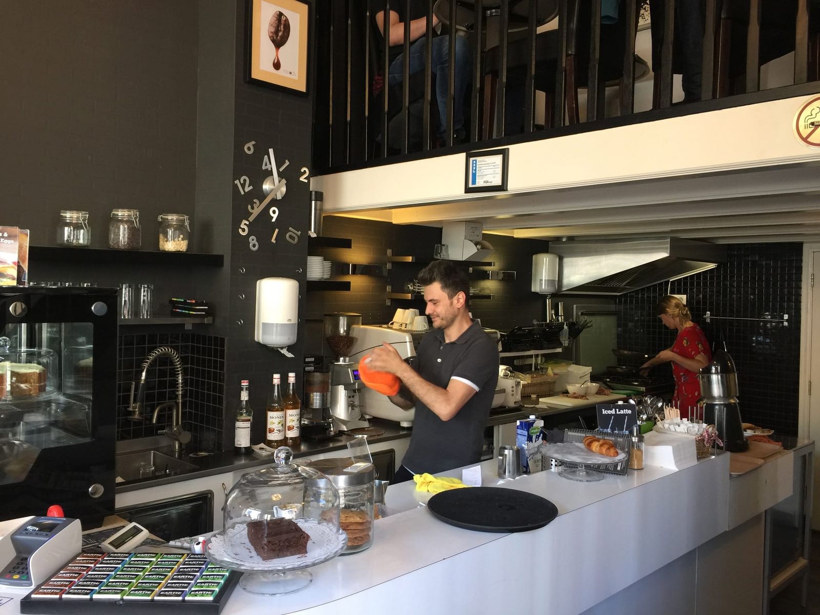 Barista in polo shirt working behind long white counter