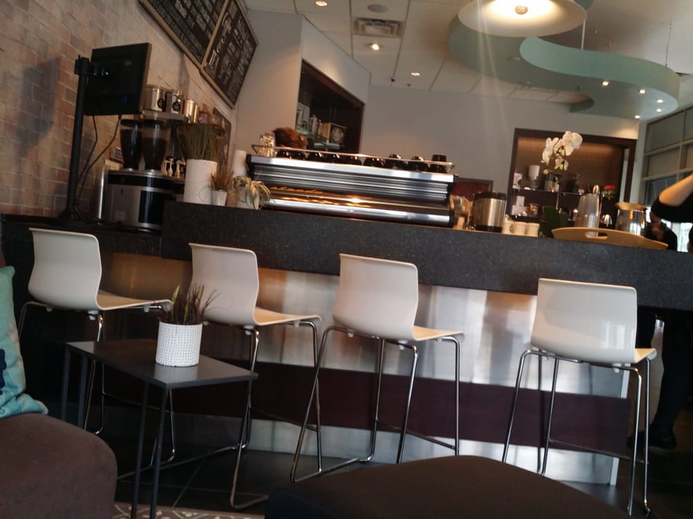 Four white stools lined along counter facing the espresso machine