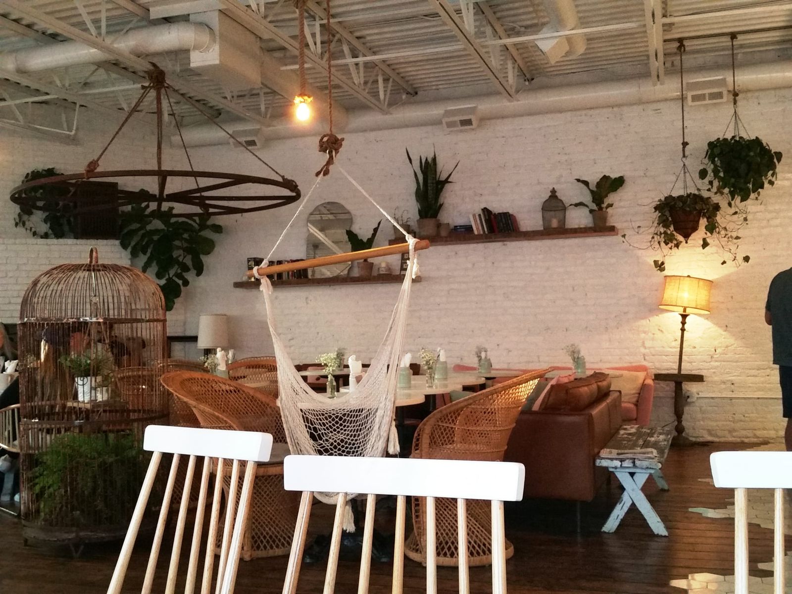 Airy white-brick room with hanging rope chair, wicker seating and potted plants