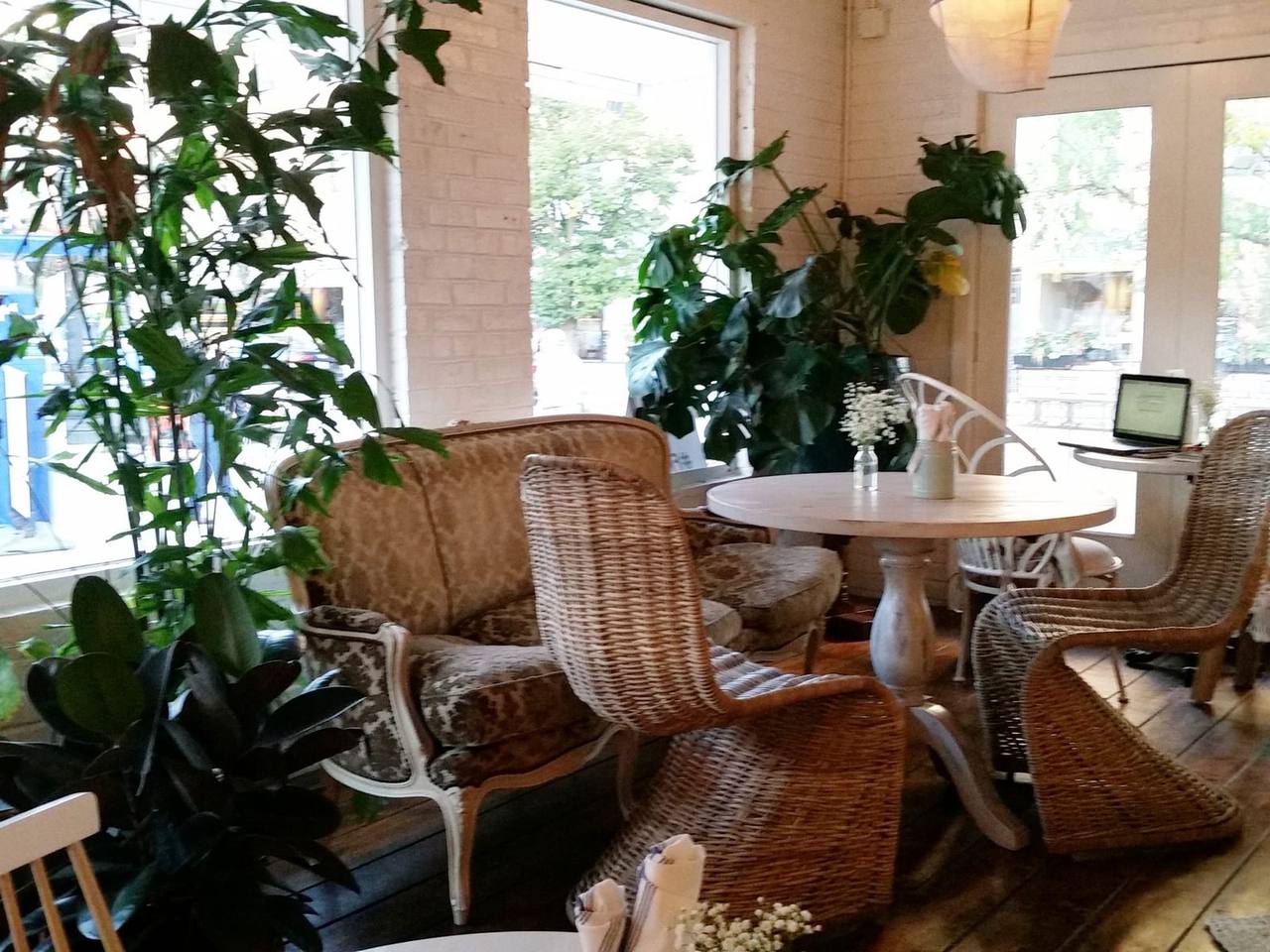 Wicker chairs and a round table by tall windows surrounded by leafy plants