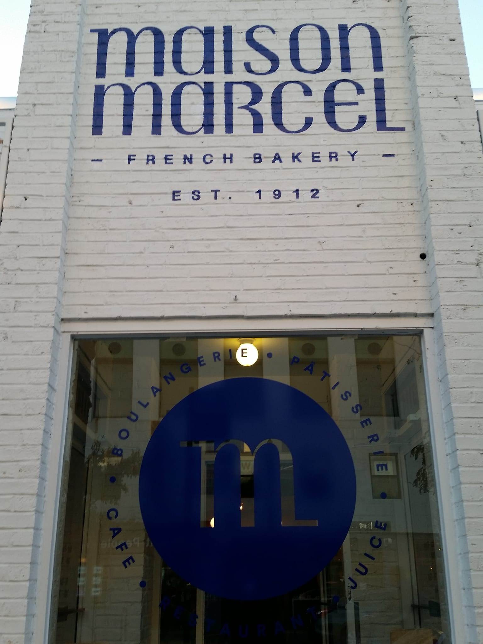 White brick facade painted with a French bakery name and a blue logo decal