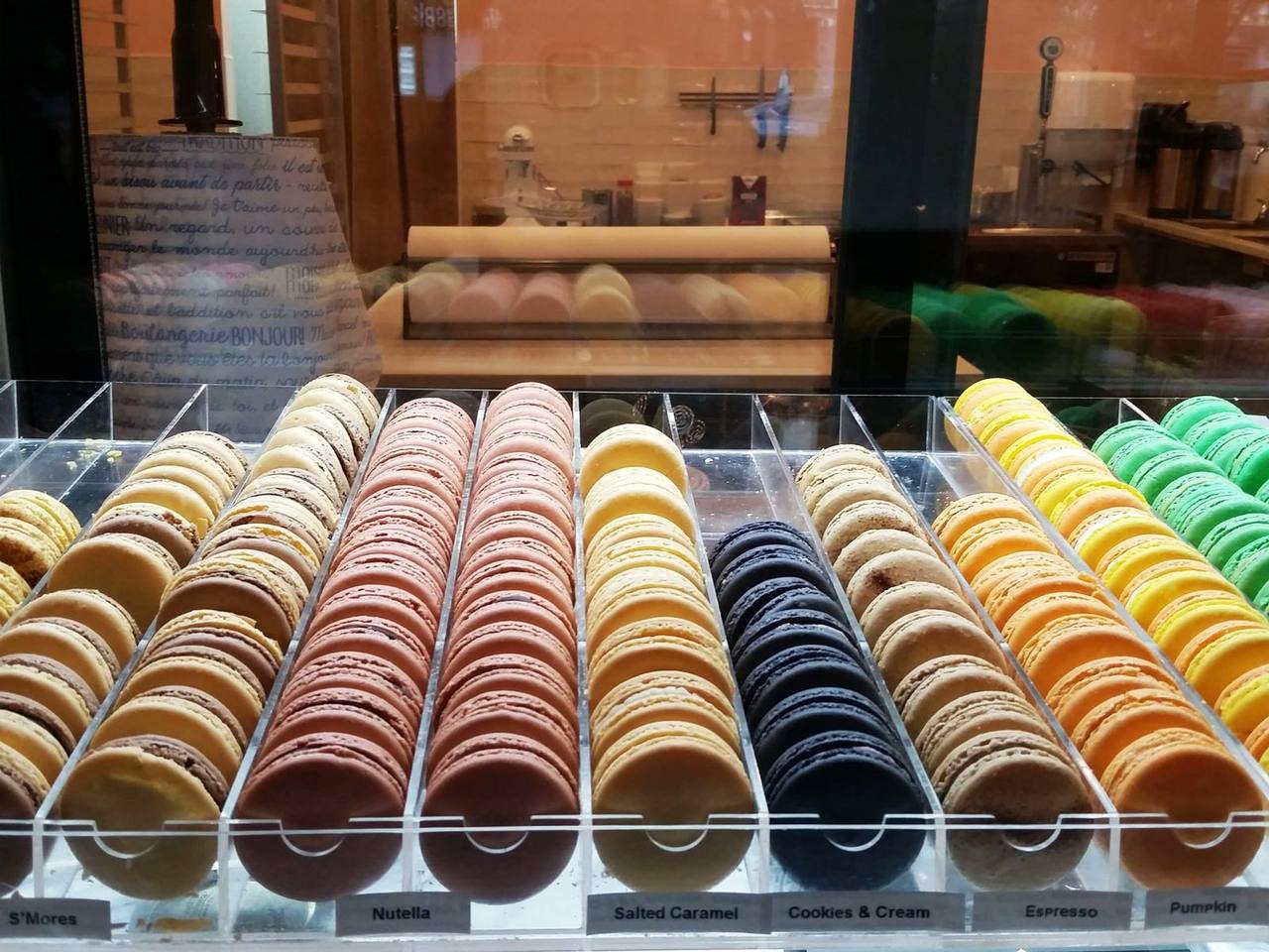 Pastry case rows of colorful macarons labeled Nutella, salted caramel and espresso