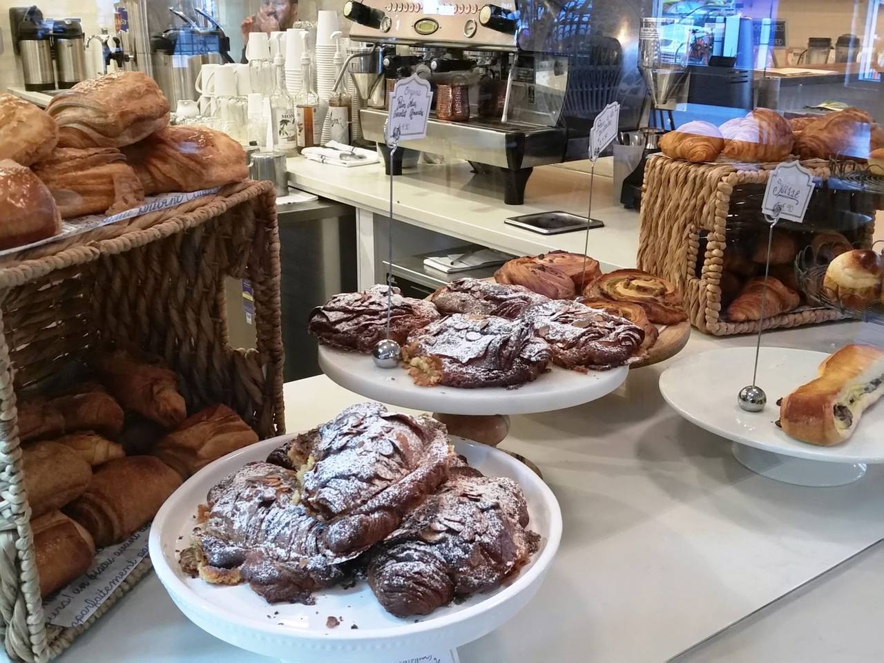 Cake stands of almond croissants and pastries in front of an espresso machine