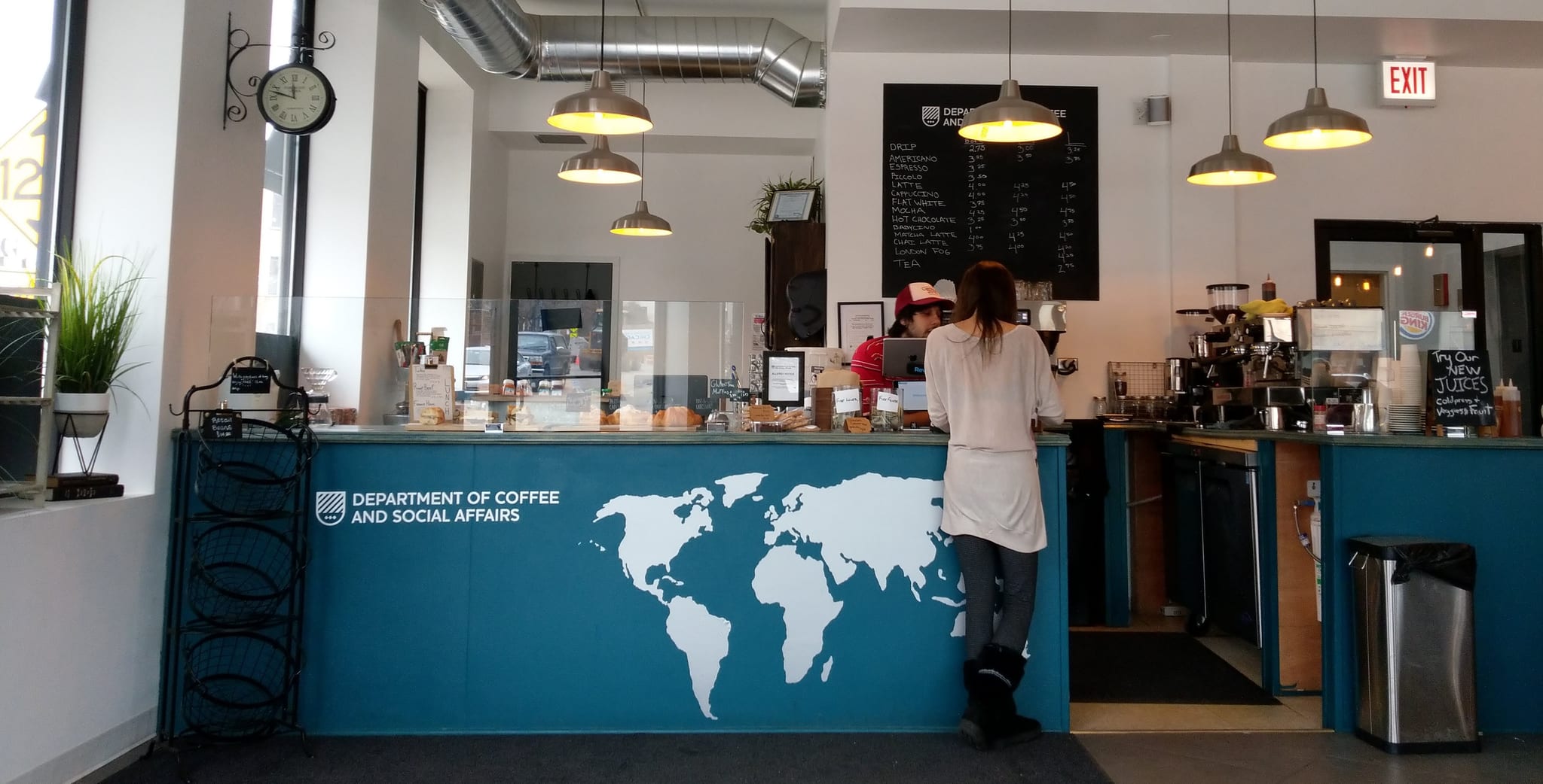 Customer ordering at a teal world-map counter under a chalkboard drinks menu