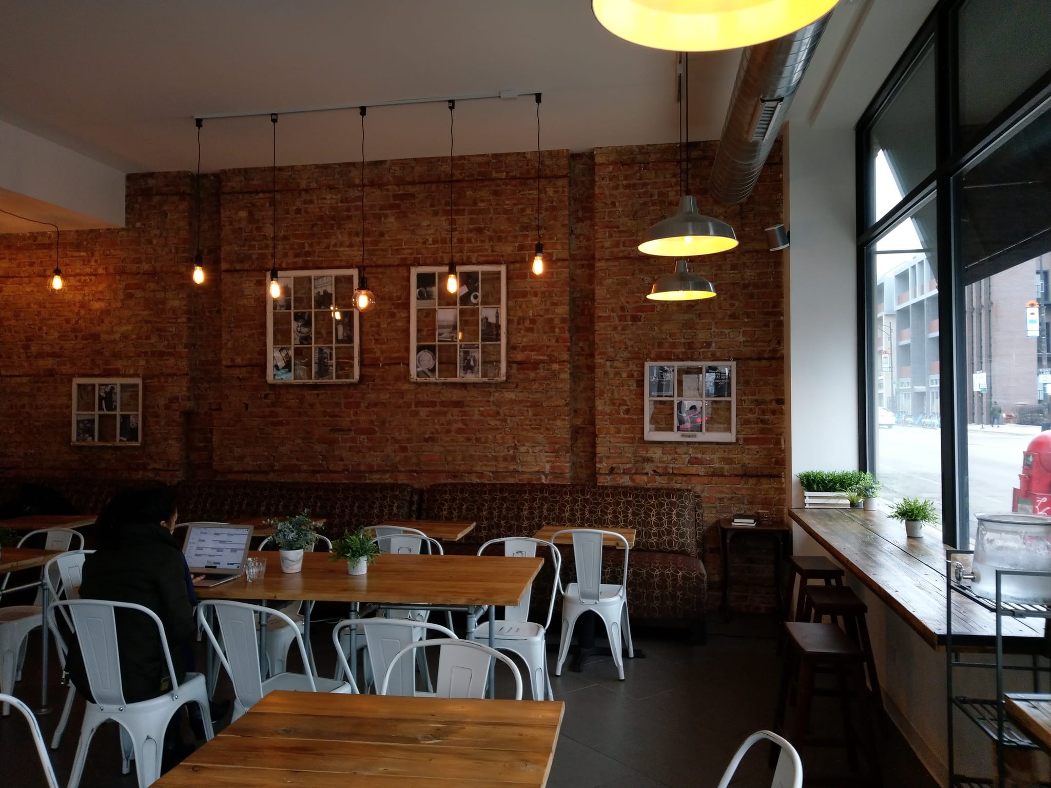 Exposed brick room with white metal chairs, wood tables and window counter seating