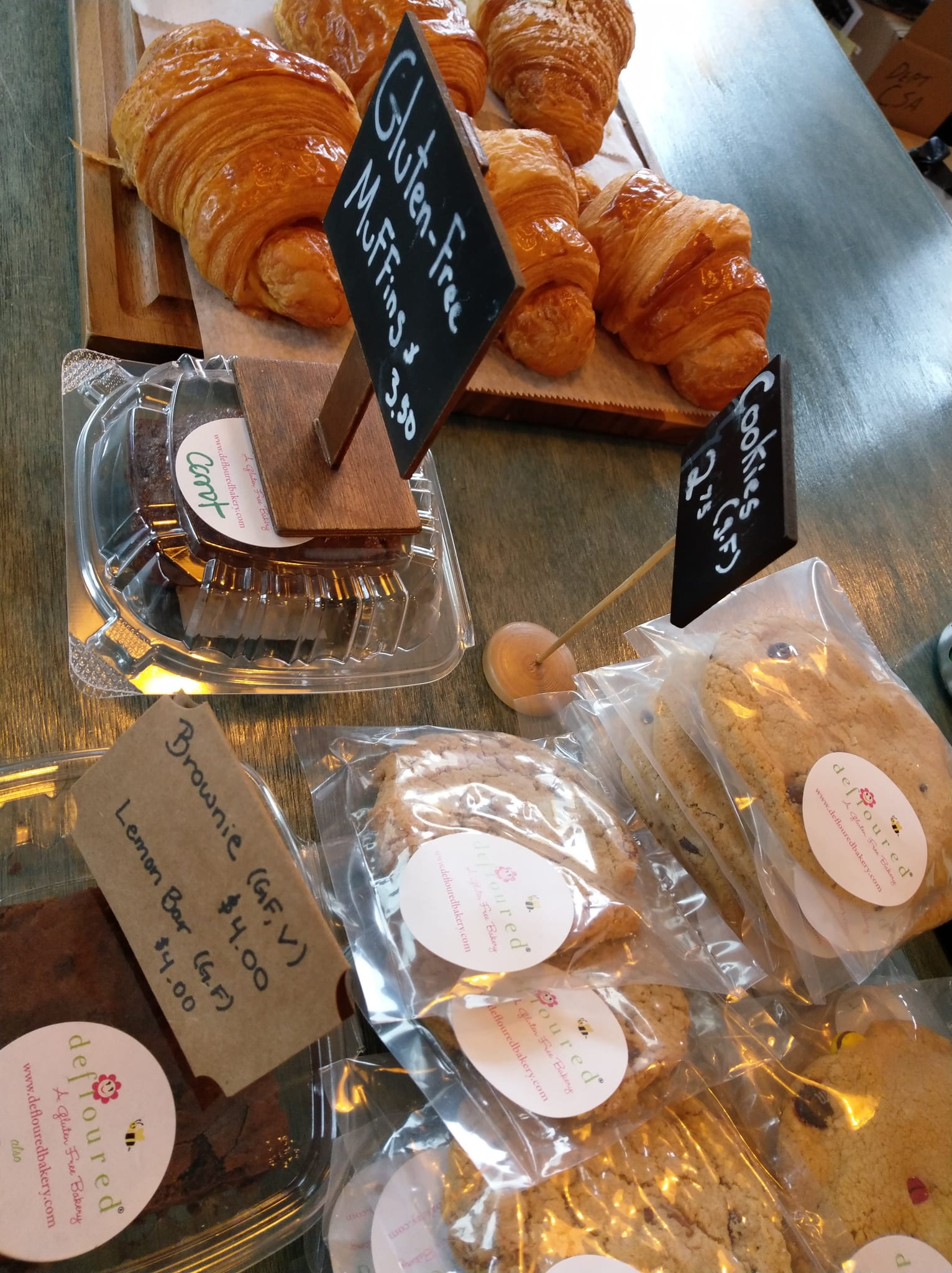 Croissants on a wooden board beside wrapped gluten-free cookies and price tags