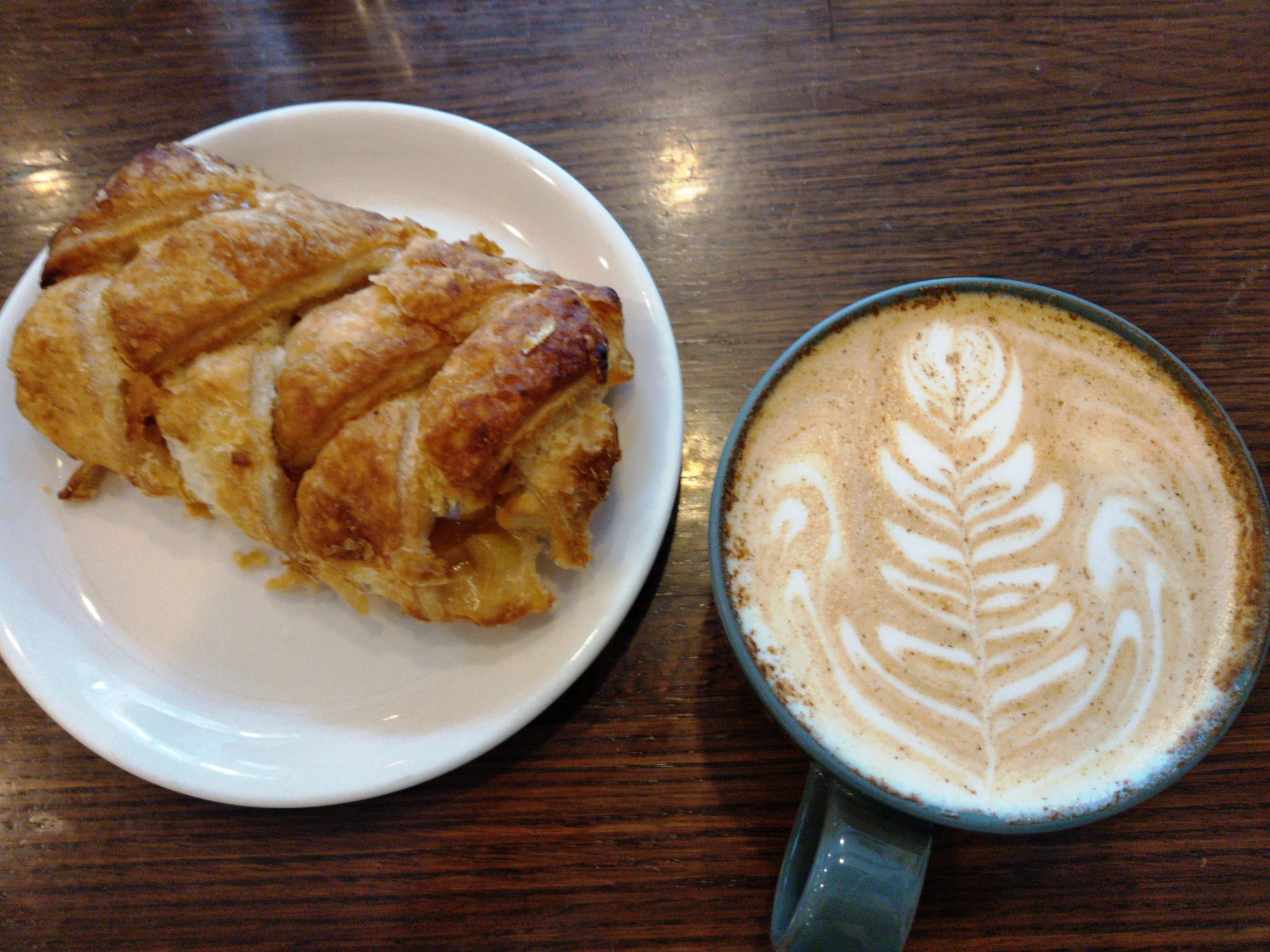Apple turnover on a white plate beside a latte with rosetta art