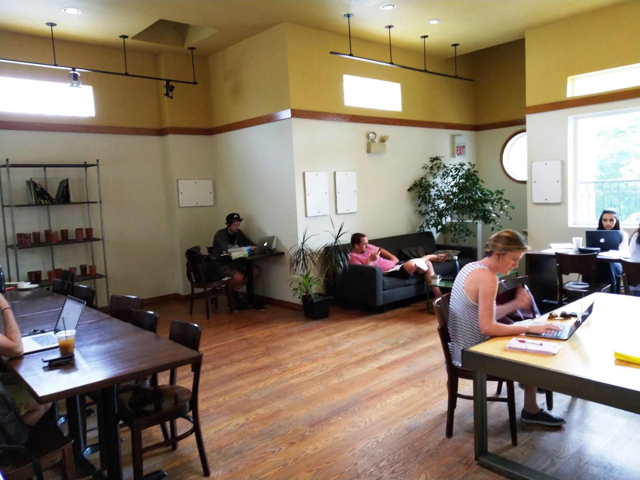 Sunny high-ceilinged cafe room with long wood tables, sofa and laptop users