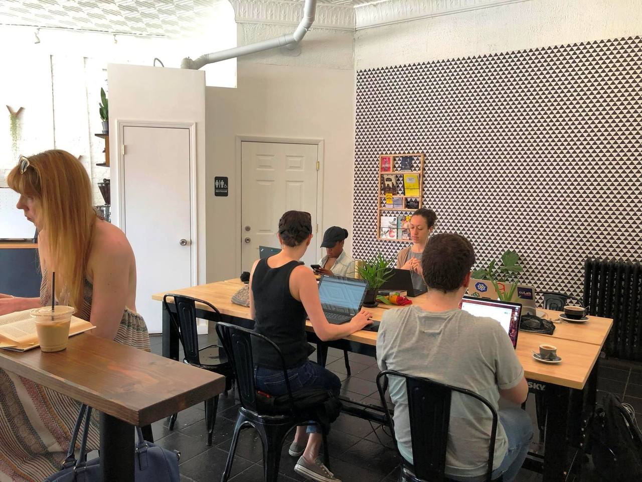 Communal wood tables of laptop workers against black-and-white triangle wallpaper