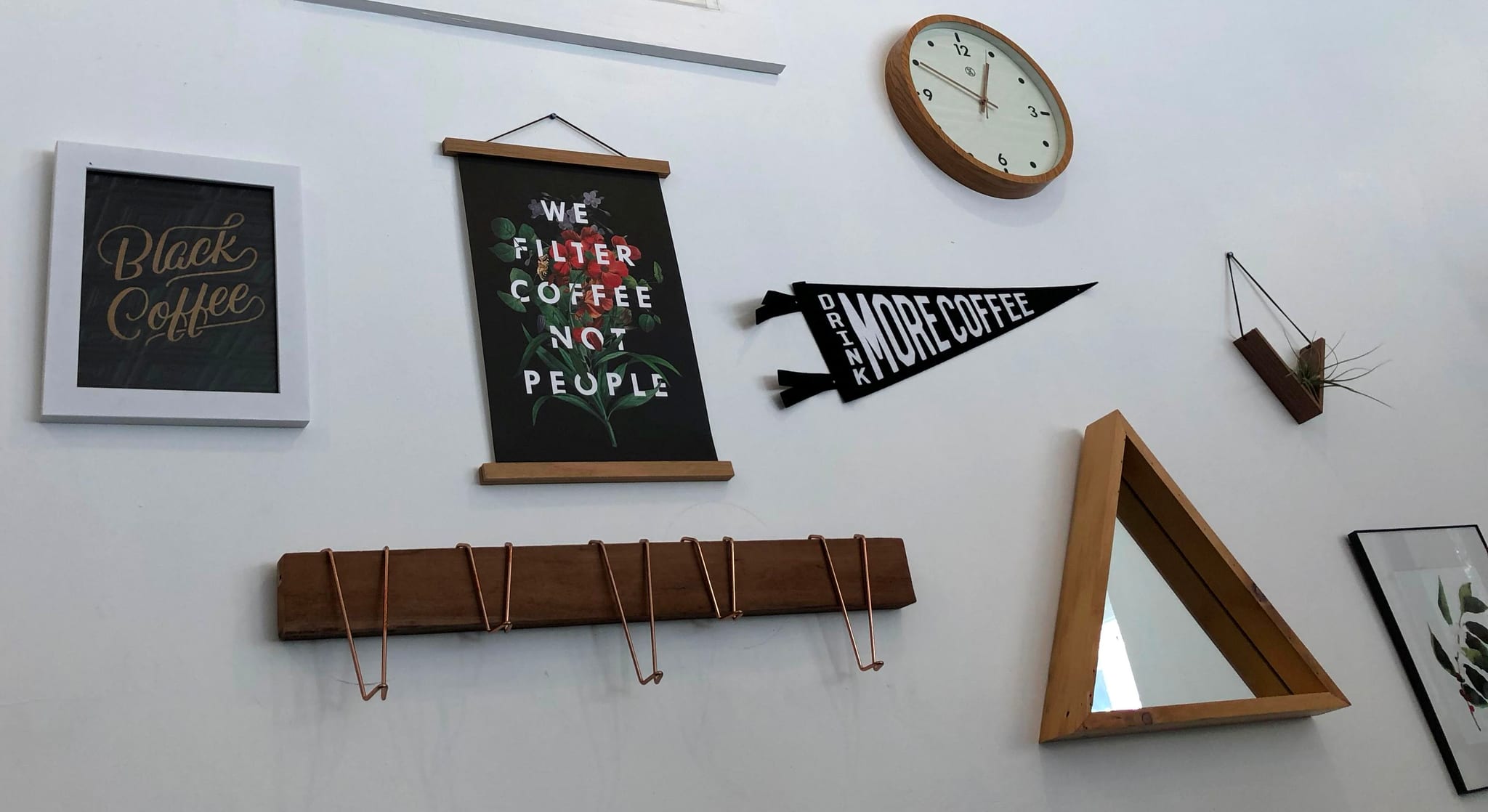 White wall gallery of coffee prints, pennant, wood clock and triangle mirror