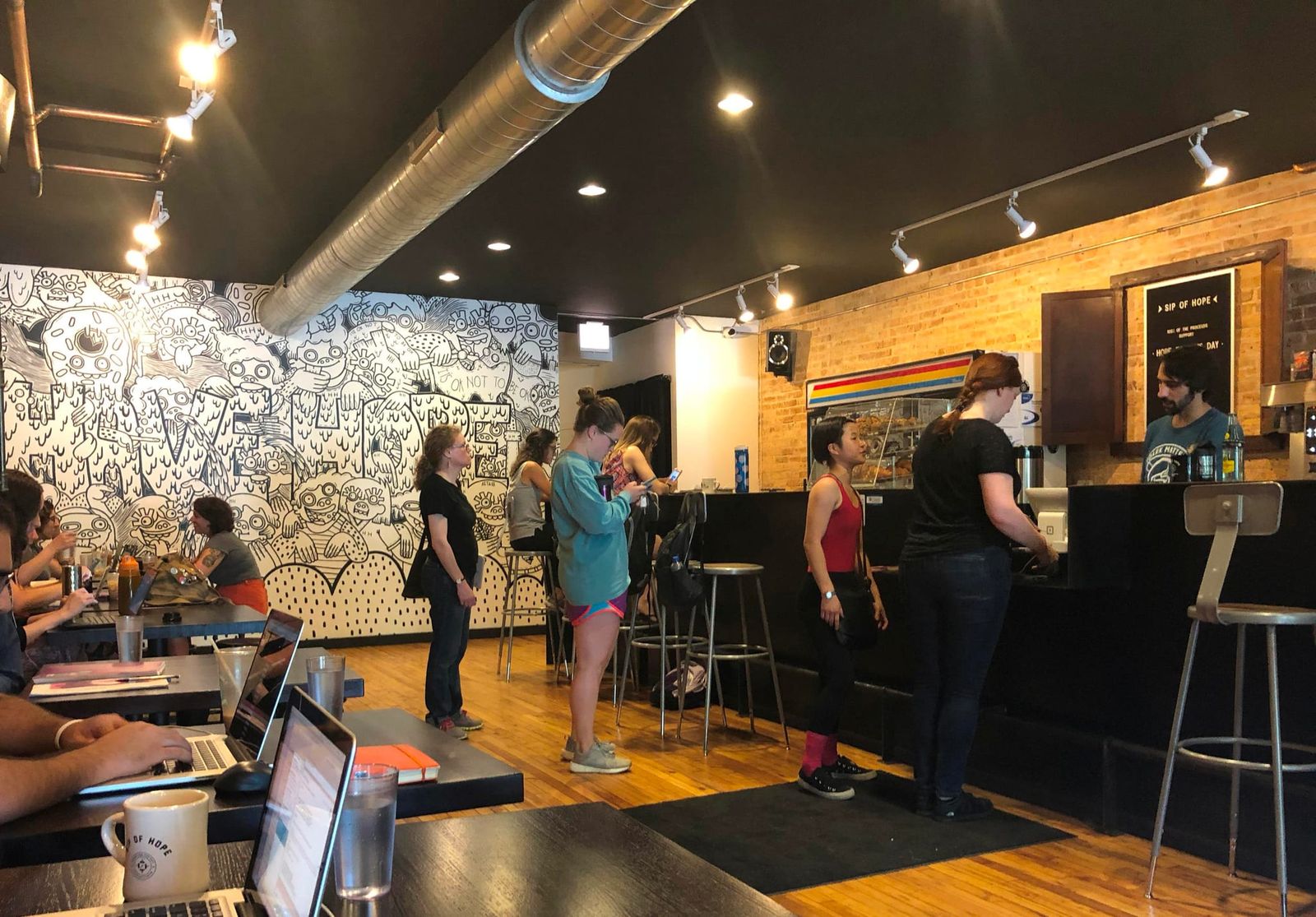Busy cafe with doodle mural, order line at counter and laptop tables