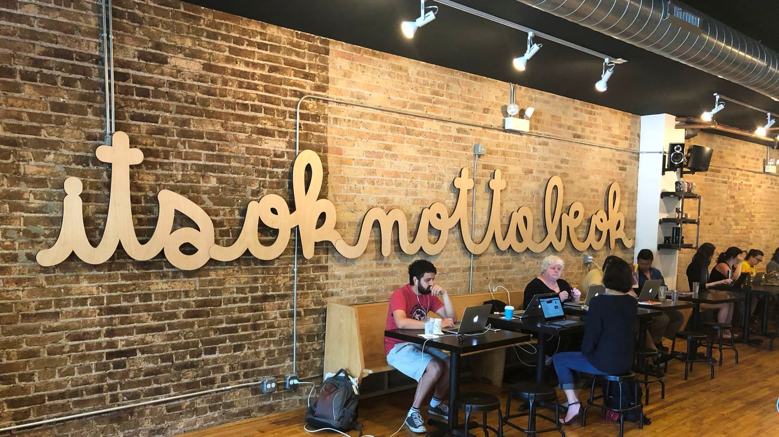 Exposed brick wall with cut wood script lettering above laptop tables