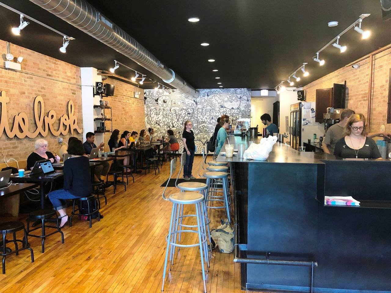 Long room with wood floors, bar stools at metal counter and mural at the rear