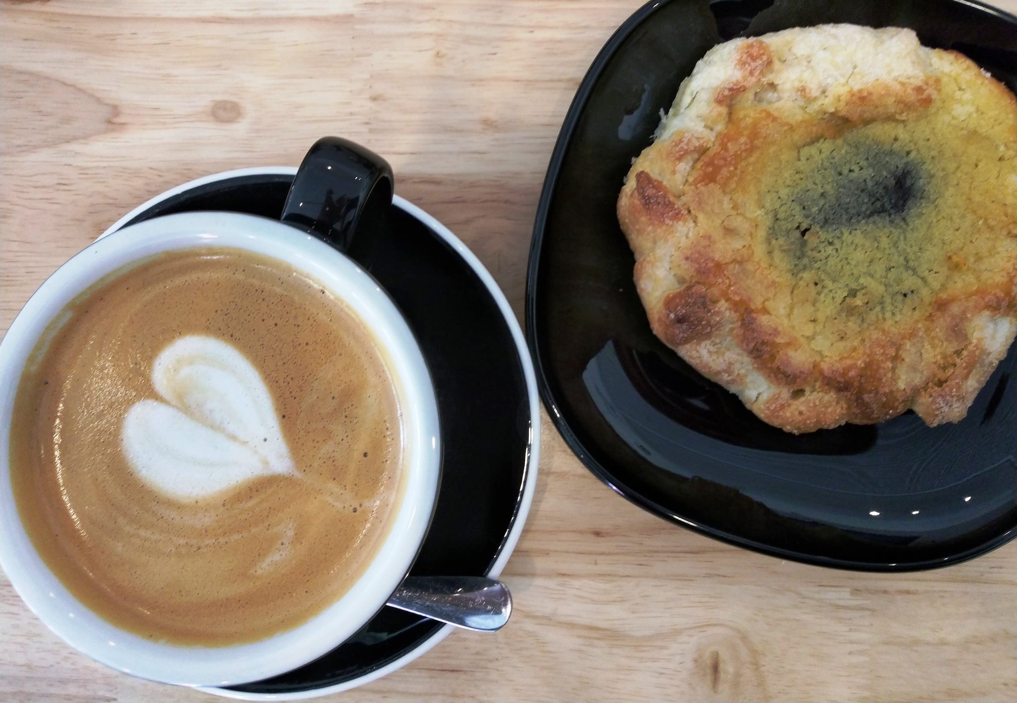Latte with heart art and a scone on black plates, light wood table