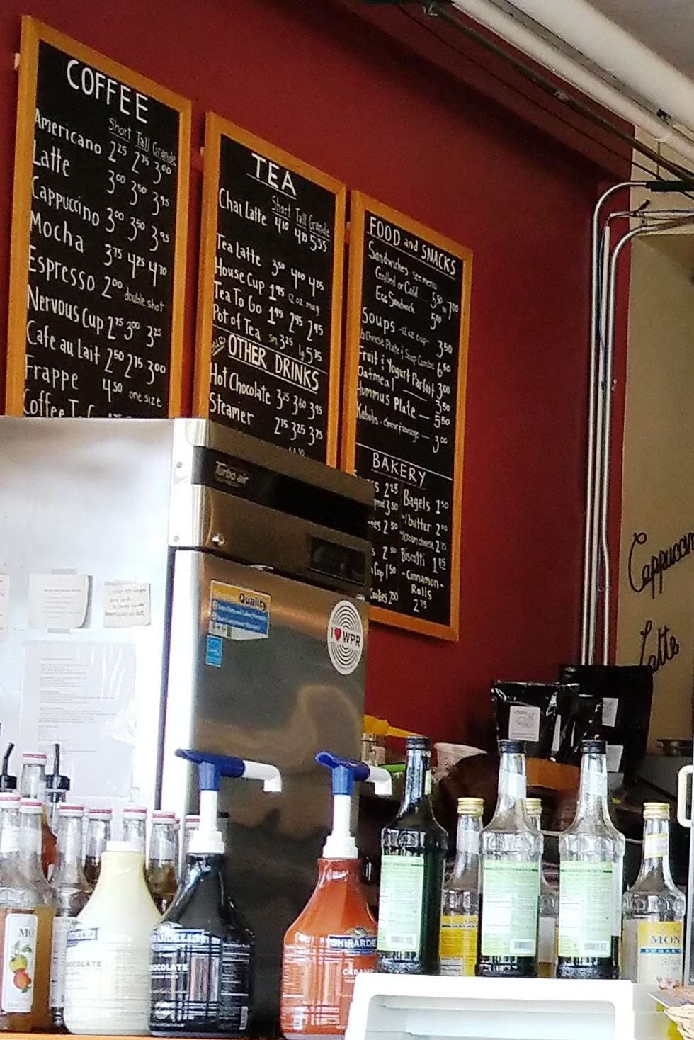 Chalkboard price boards above rows of flavored syrup bottles