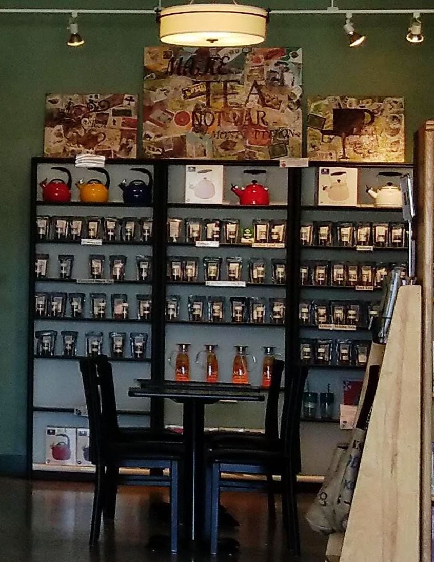 Shelves of loose leaf tea jars and colorful kettles behind a table