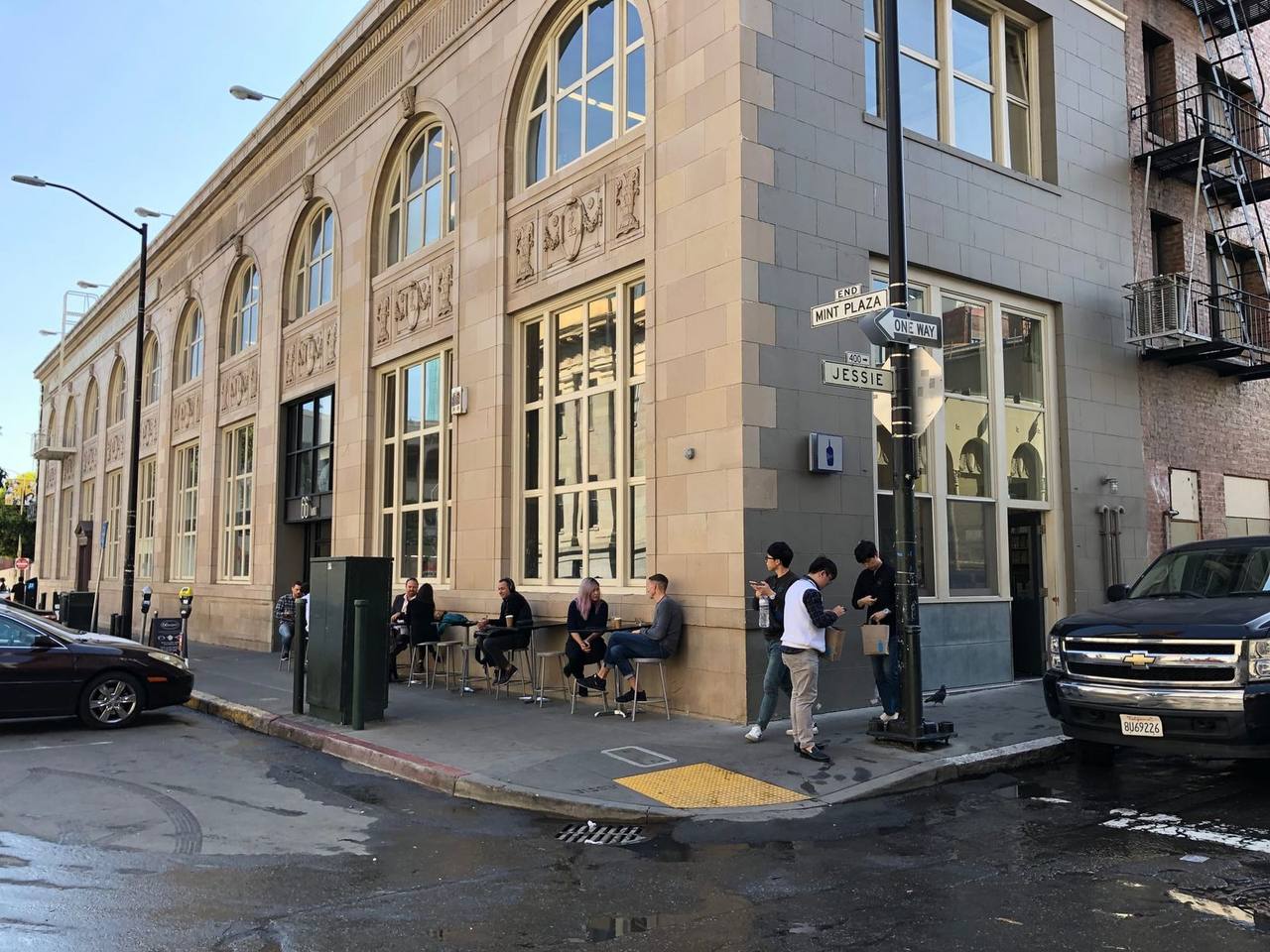 Stone corner building at Mint Plaza with sidewalk stools and street signs